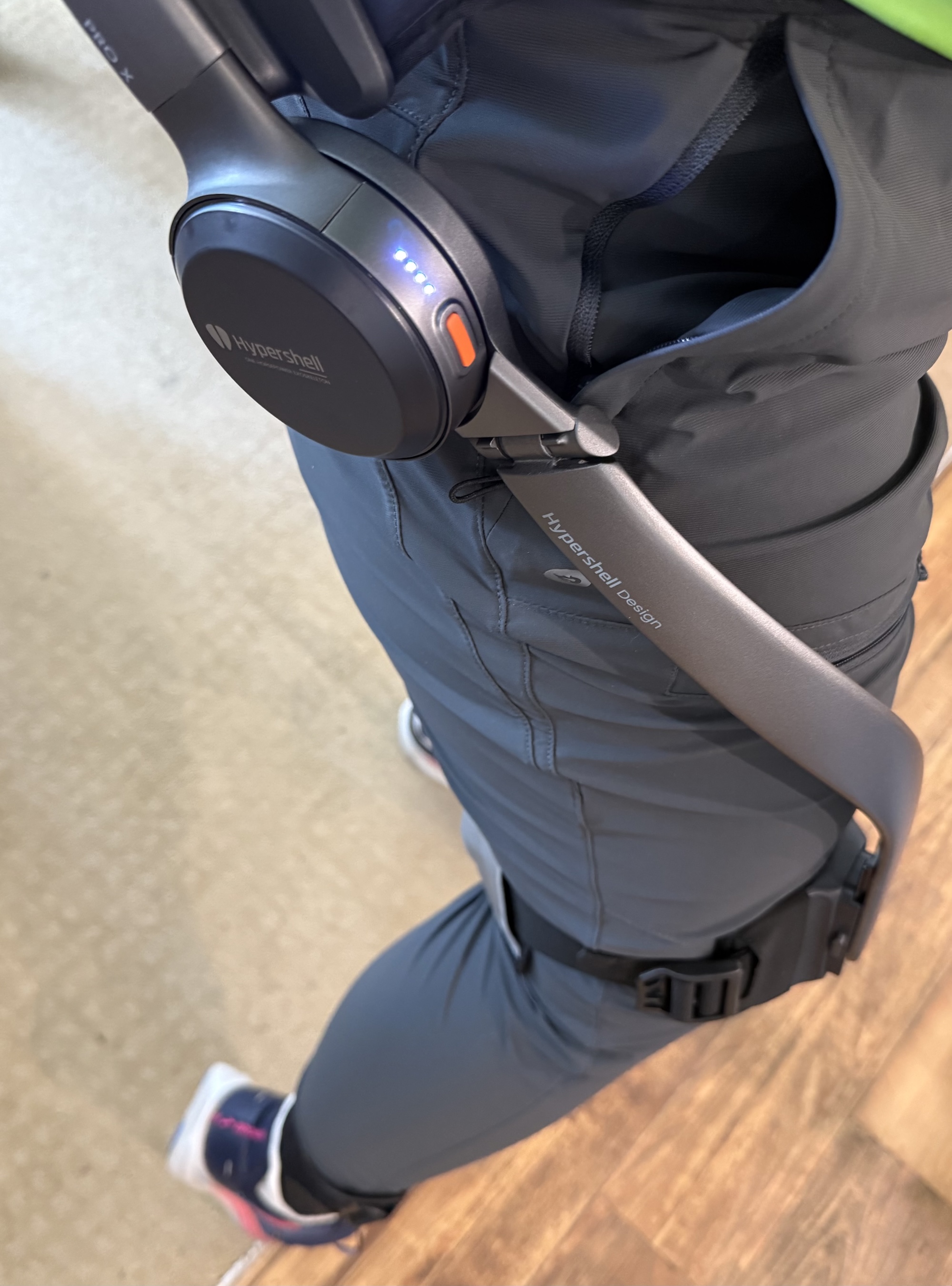 A Hypershell Pro X model worn over grey loose-fitting pants. This is a side view, so you can see the motor against my hip, the bar as it wraps around toward the front bottom of my leg, and the knee strap. 